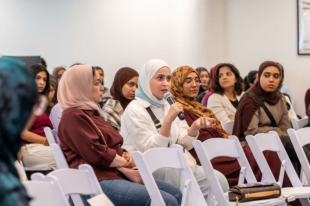 A woman asks a question to panelists out of frame with an audience of other women