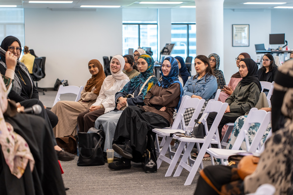 Muslim women sit in mulitple rows listening to a presenter out of view